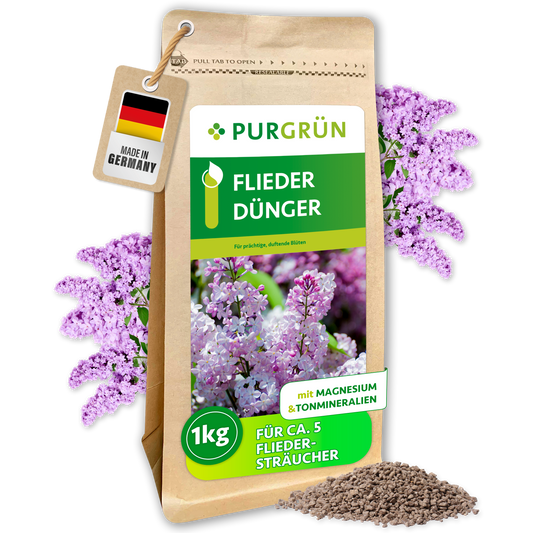 Purgrün Fliederdünger im 1-kg-Papierbeutel, umgeben von Fliederblüten und feinem Granulat; reicht für ca. 5 Fliedersträucher.