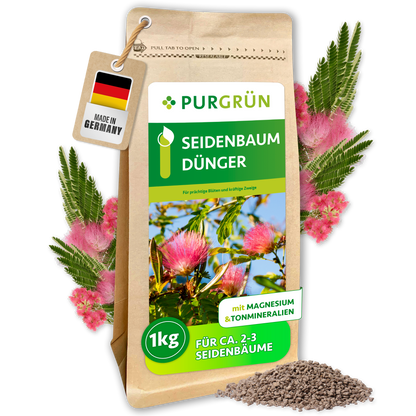 Purgrün Seidenbaum-Dünger, 1 kg, mit Magnesium und Tonmineralien, umgeben von rosa Seidenbaumblüten und Granulat.